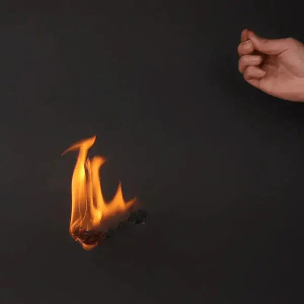 Hand holding burning flash paper producing bright orange flame against black background